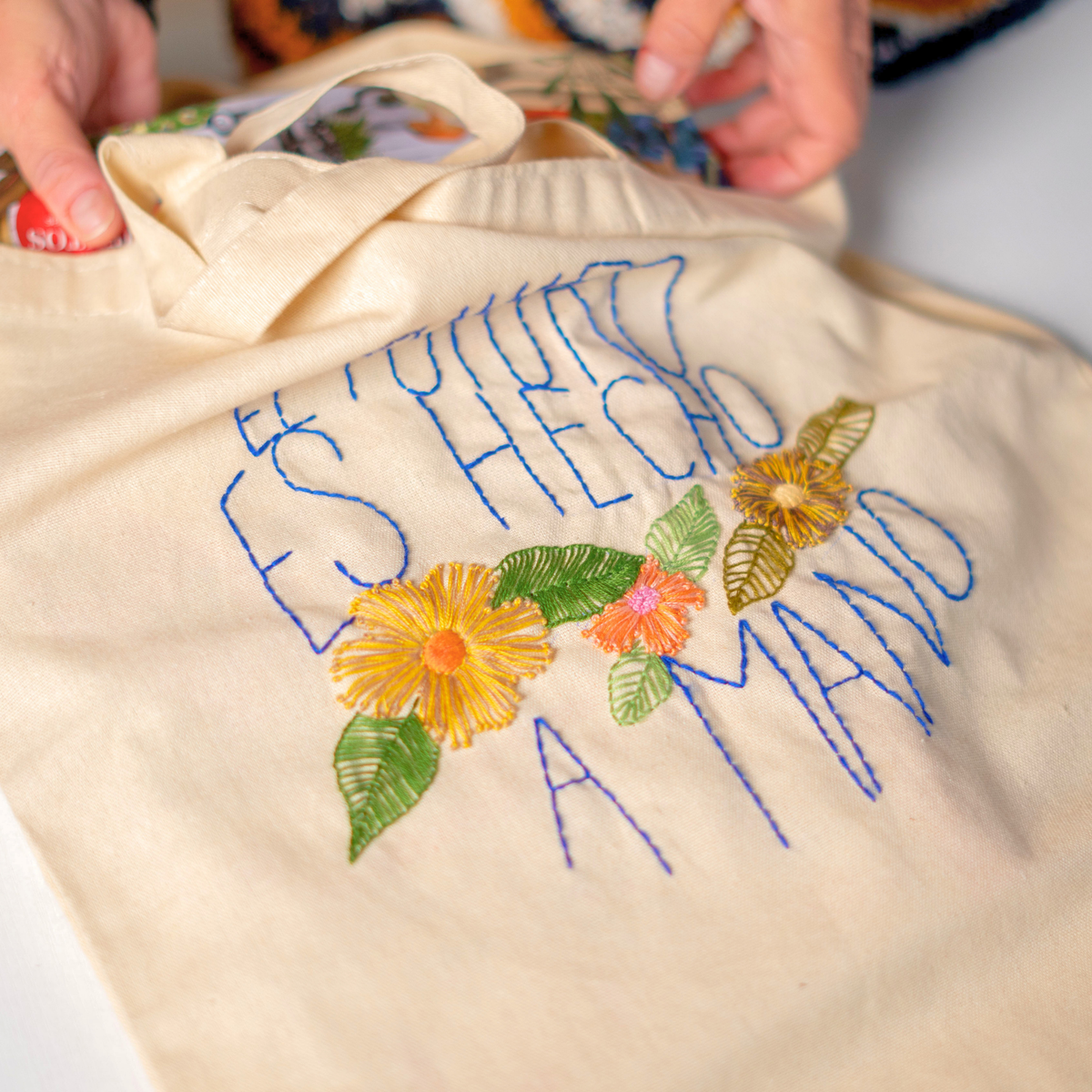 Totebag con la frase «El futuro es hecho a mano» bordada en azul, con flores de colores