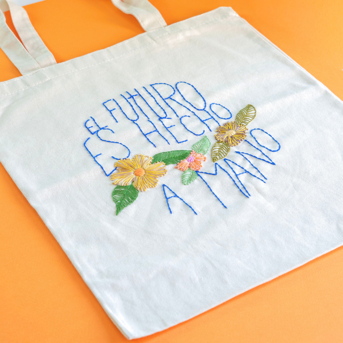 La frase bordada terminada, con flores amarillas, naranjas y verdes